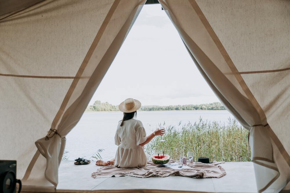 Zena na terasi glamping satora sedi uz reku i uziva.