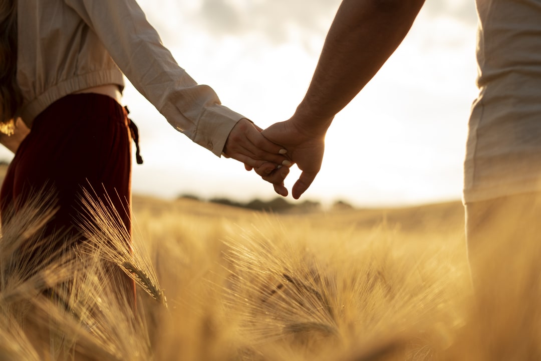 Muz i zena se drze za ruke u polju psenice.